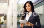 An elegant and smiling business woman holding a table inside a bright business office