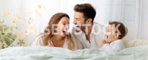 Happy couple with their child laughing in the morning over a bed